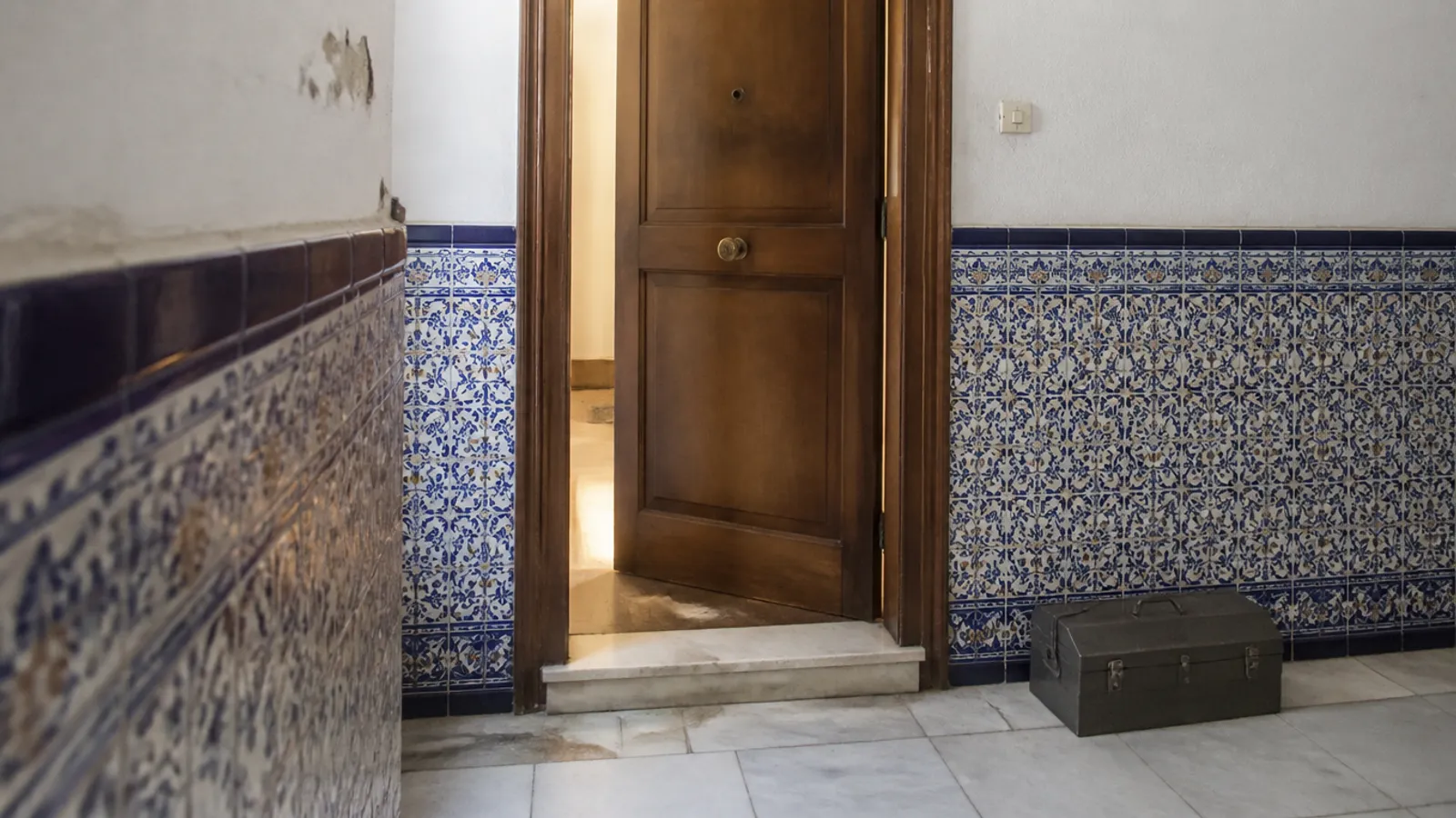 Cerrajero de espaldas abriendo la puerta de una vivienda en Utrera con linterna sobre el bombín